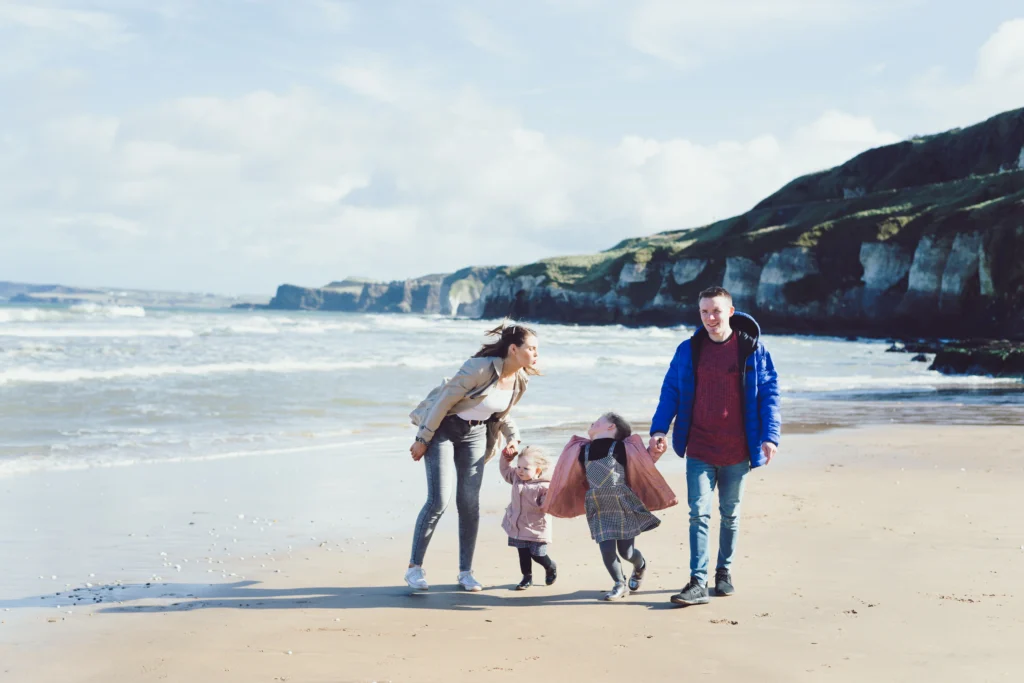 Northern Ireland family photographer captures parents and two children playing and laughing on a windswept beach with cliffs