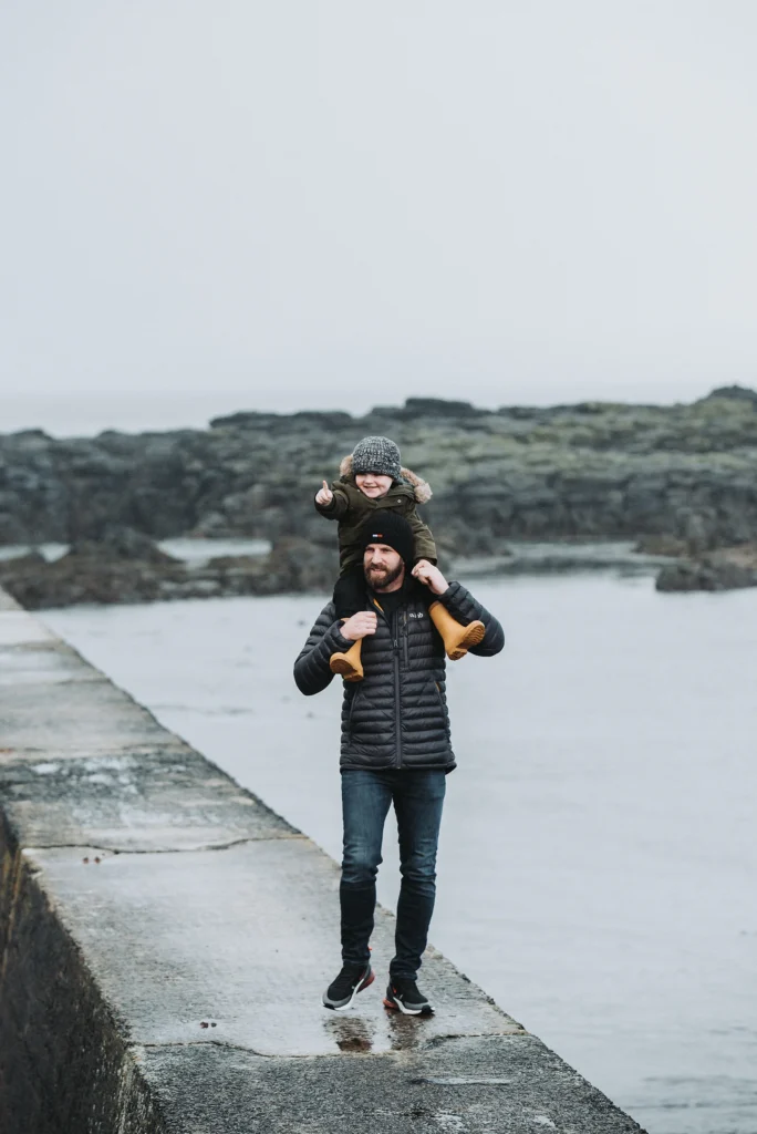 Northern Ireland coastal family portrait of father carrying smiling child on his shoulders during outdoor fun session
