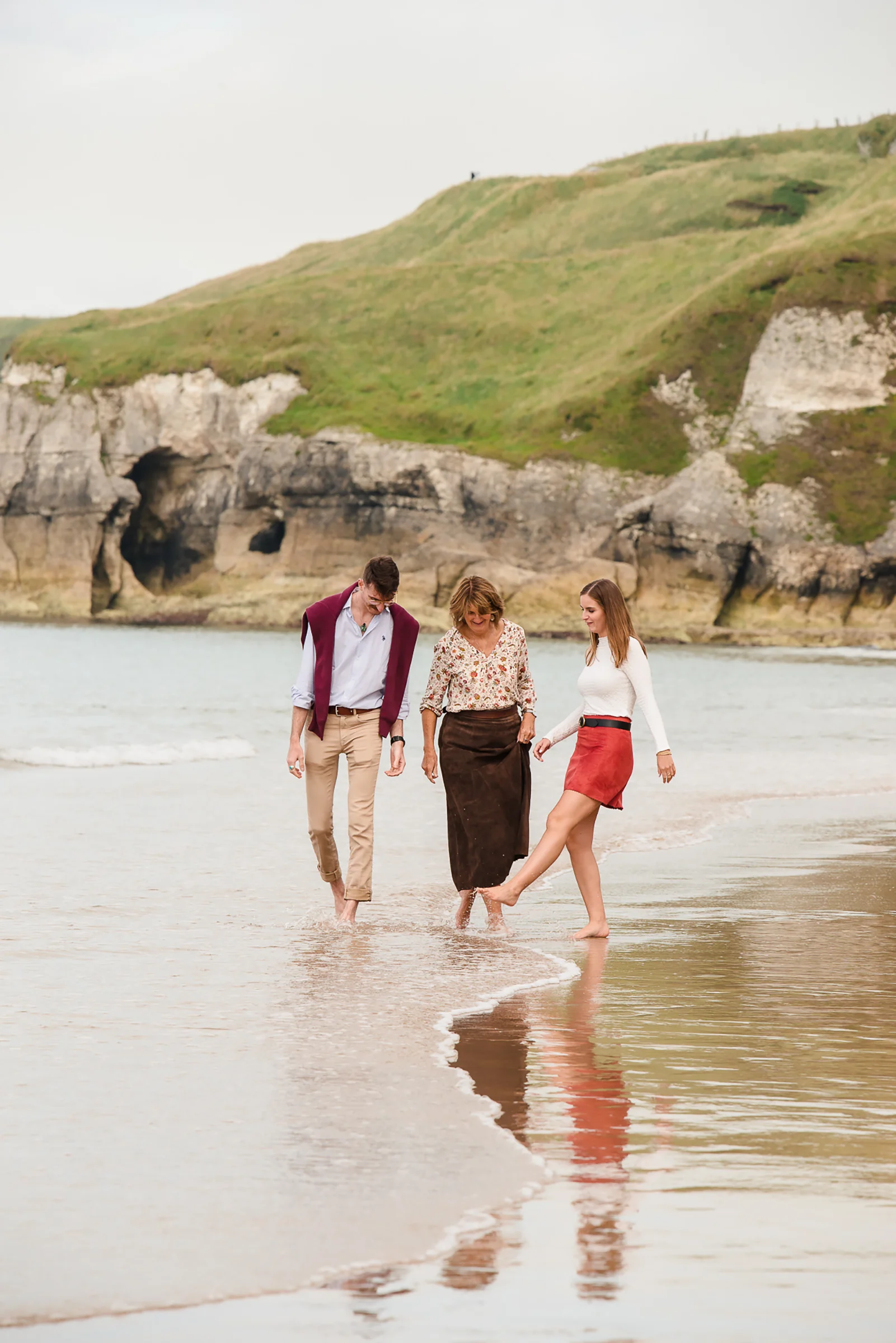Northern Ireland family photographer outdoor portrait: three family members walking and splashing on a sandy beach shore