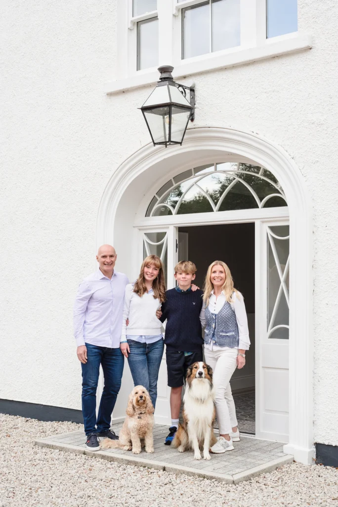 Happy Northern Ireland family portrait outside white home with two dogs, casual outdoor family photography session