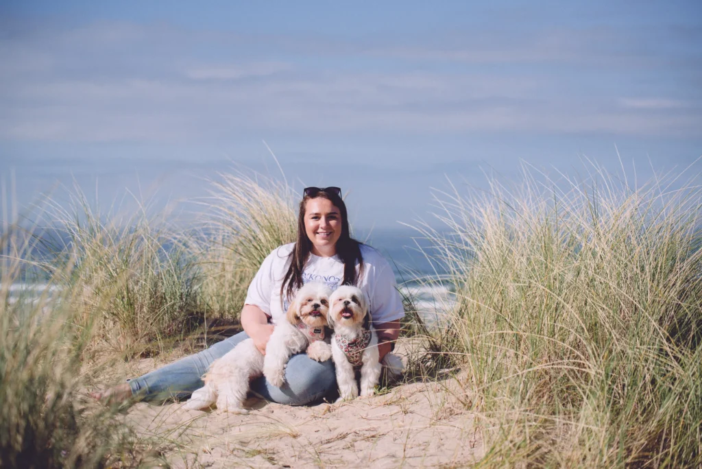 Woman sitting on coastal dunes in Northern Ireland holding two small dogs for a relaxed outdoor family portrait